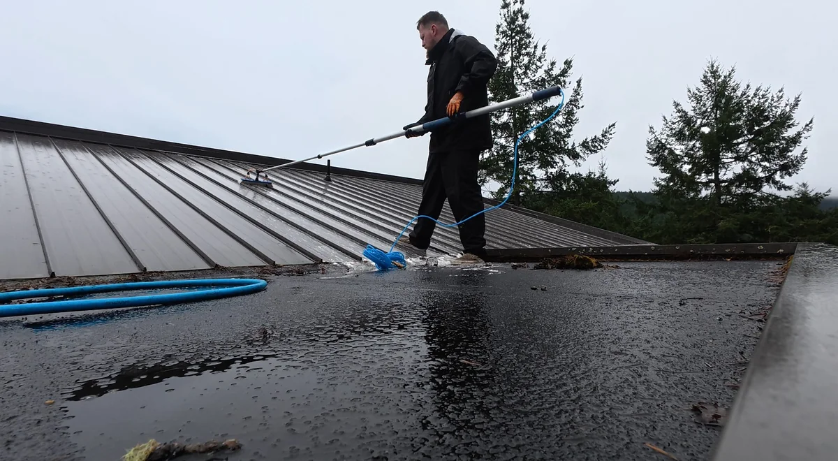 Exterior-care work with a long-handled brush on a wet metal roof